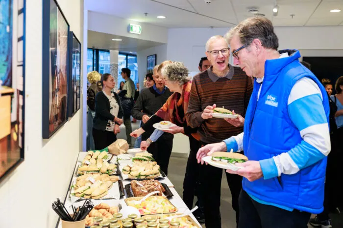 Mensen pakken broodjes en hapjes tijdens een bijeenkomst in een kantoorruimte.